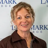 Karrie Kalich stands in front of a white background featuring the Landmark College name and logo. 